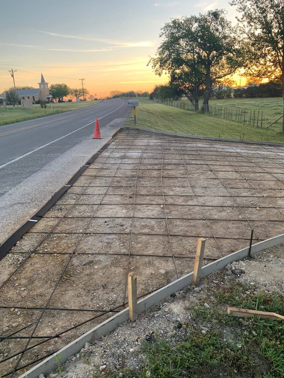 Concrete mixer truck pouring a driveway approach near a rural church at sunset