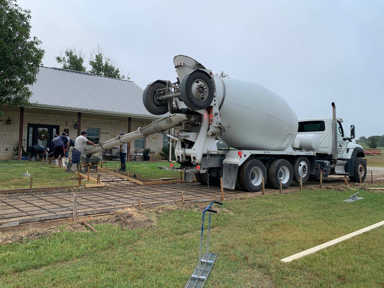 Concrete mixer truck pouring a new walkway beside a Hill Country stone home