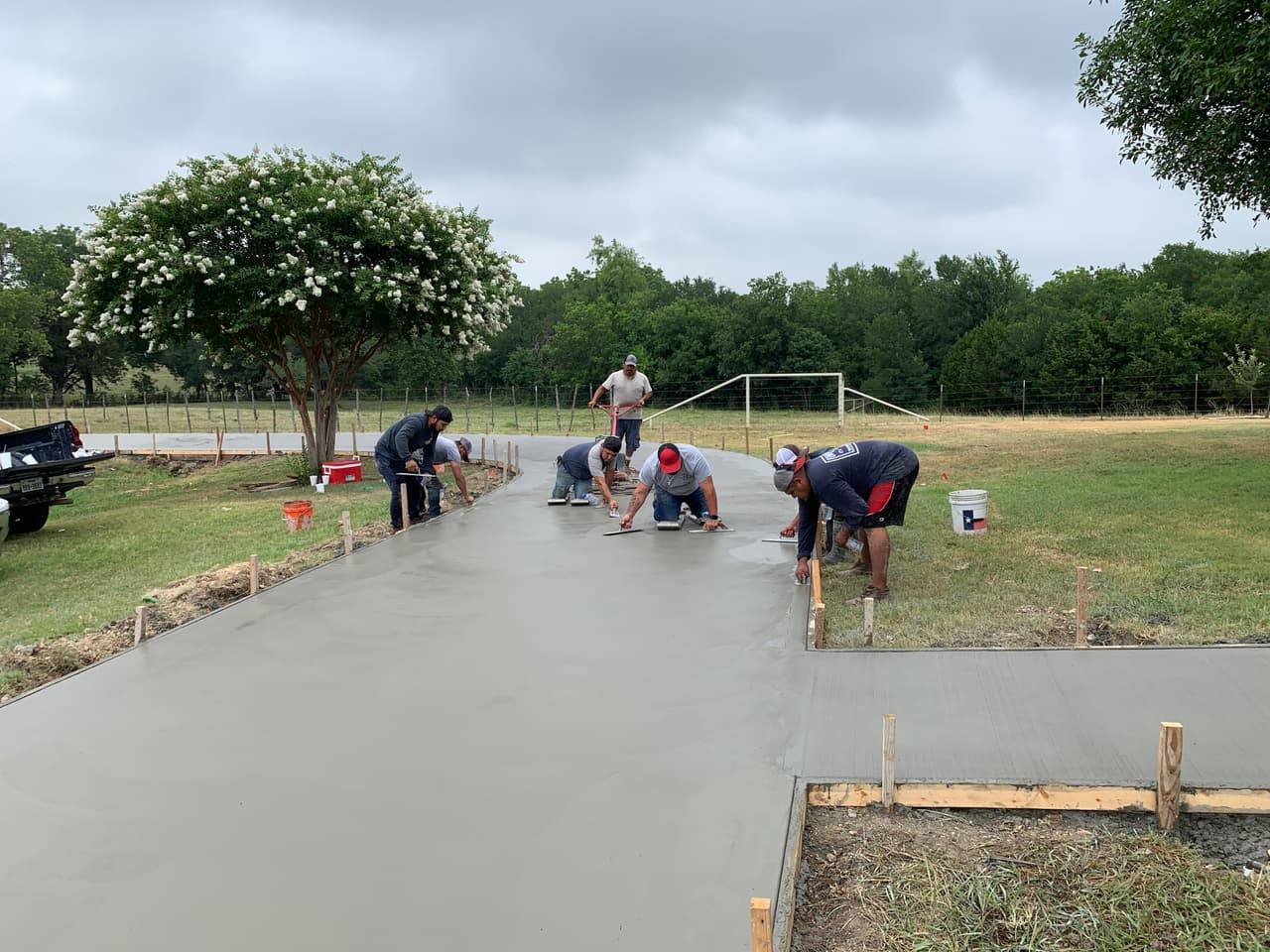 Crew finishing a freshly poured curved concrete driveway with hand trowels in the Highland Lakes area