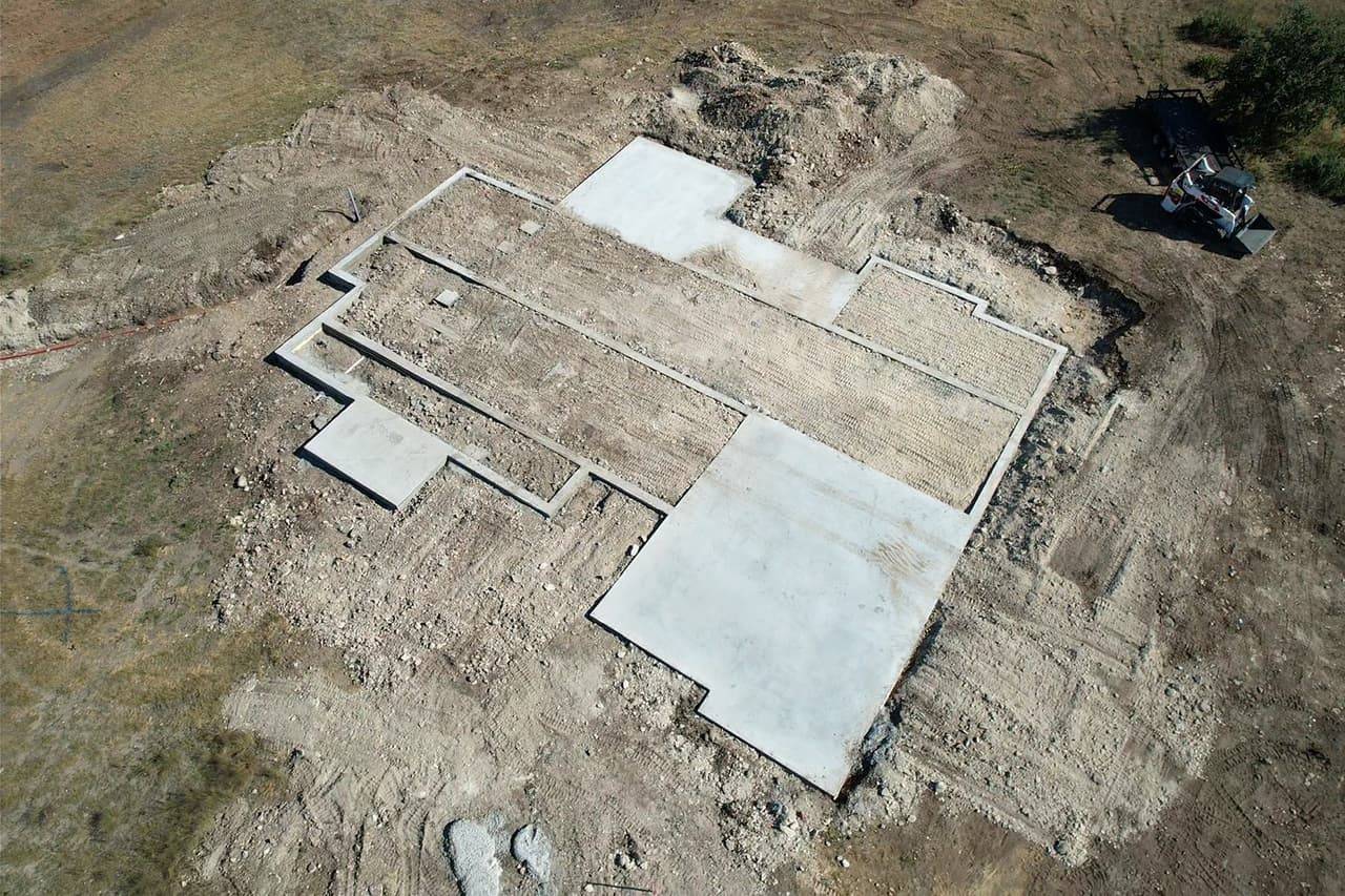 Aerial view of a poured concrete foundation with multiple connected sections on a rural lot