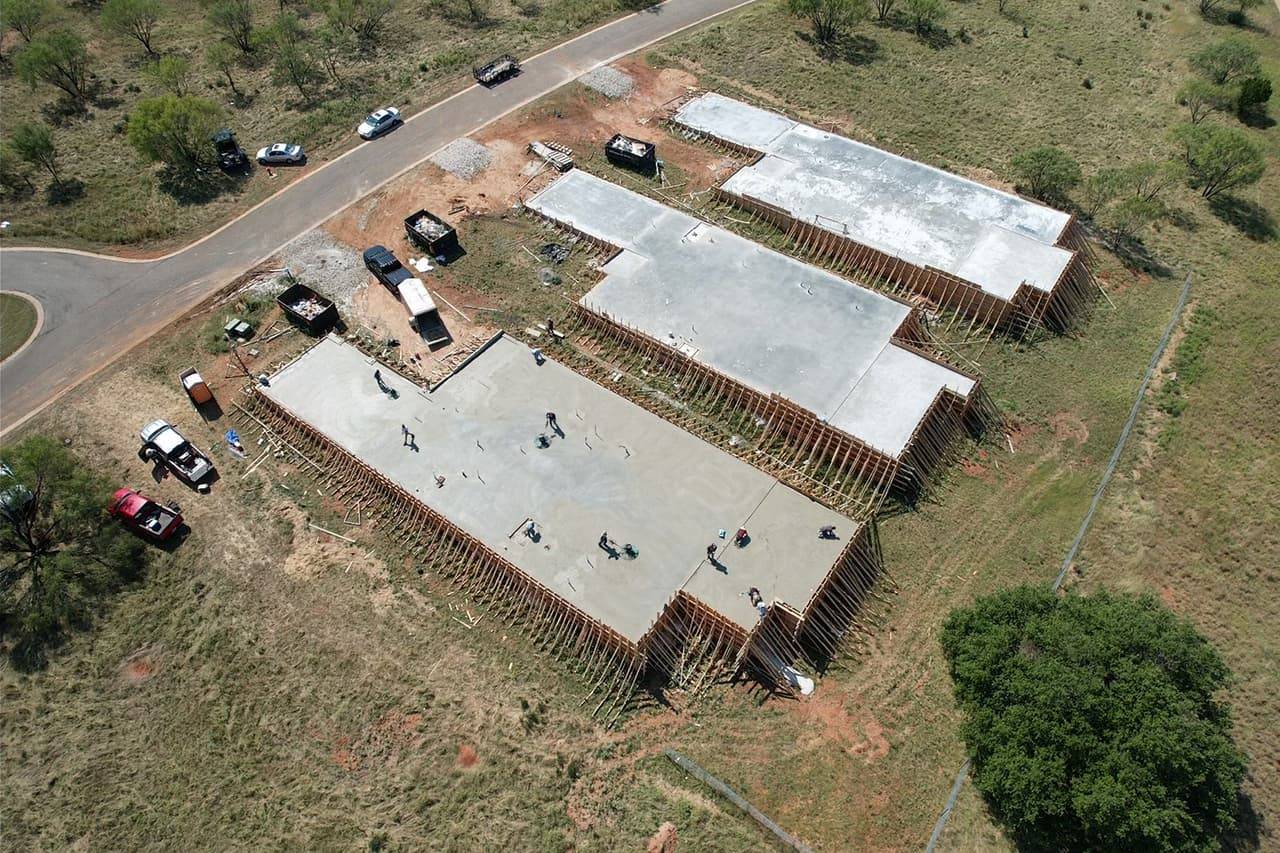 Aerial view of a large reinforced concrete building pad poured on a rural lot near a golf course