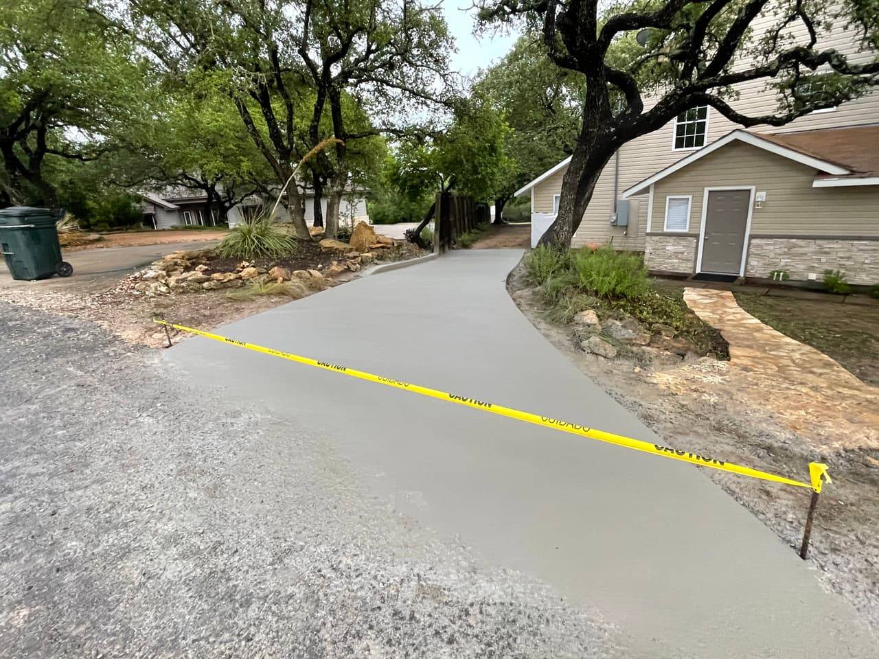 Finished concrete driveway curving past landscaping and tying into a stone walkway at a residential lot