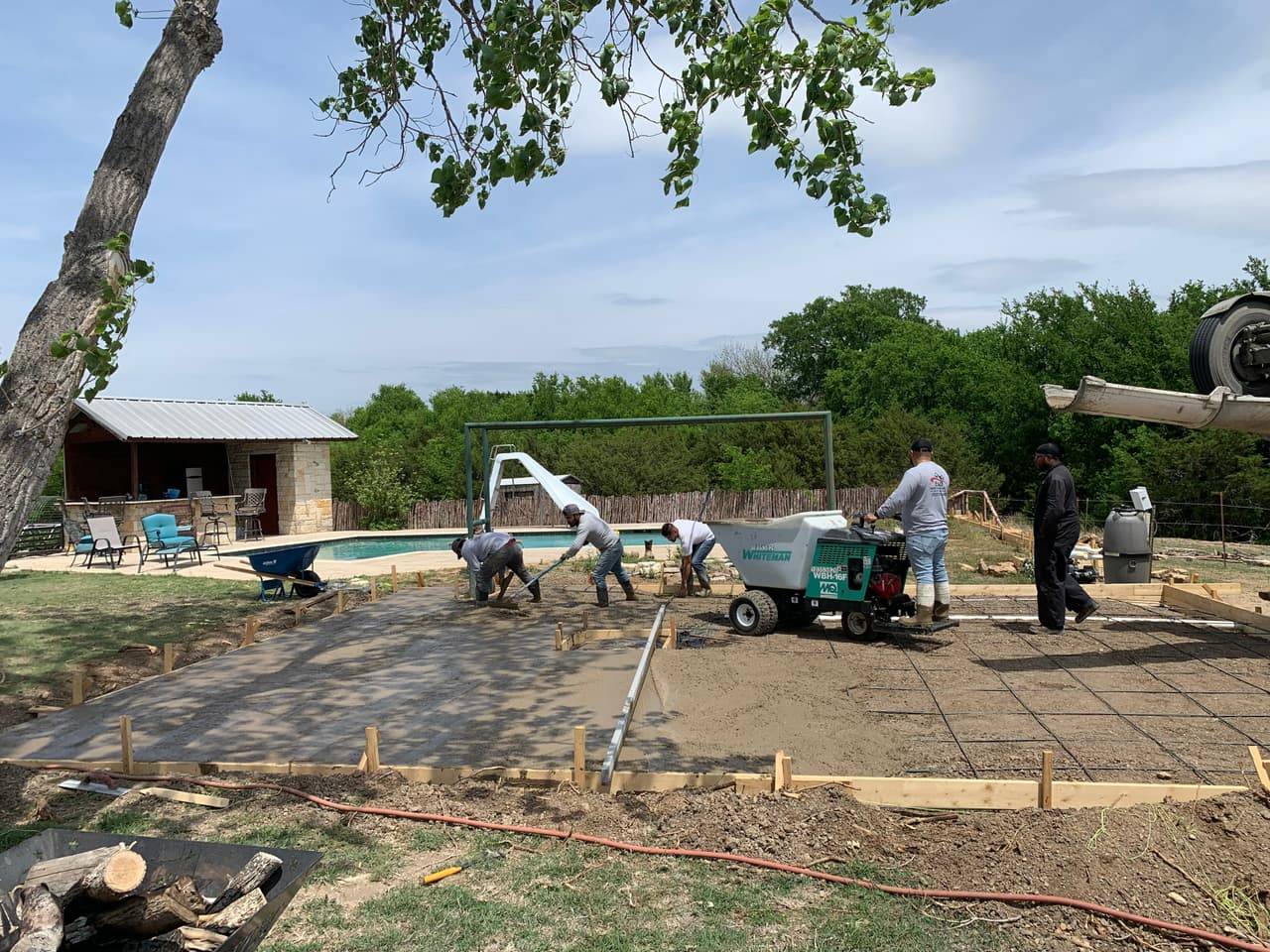 Concrete mixer truck and crew pouring a reinforced slab on a shaded rural property